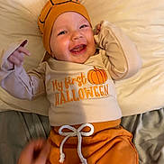 Jacob joined the competition — help win amazing prizes! baby, child, smiling, halloween, pumpkin, hat, orange_clothing, beige_clothing, bed, blanket, cute, happy, infant, lying_down, indoor, face, person, celebration, festive, holiday