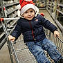 child, boy, shopping_cart, santa_hat, jacket, jeans, smile, aisle, store, shopping, holiday, winter_clothing, footwear, indoor, metal, retail, person, cute, happy, casual