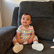 Ariella is registered to the contest to win money with this photo: baby, casual, child, comfortable, cozy, curious_expression, cute, floor, furniture, gray_chair, happy, indoor, infant, person, portrait, sitting, soft_light, striped_clothing, white_shoes, young_child