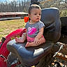 baby, barn, child, clouds, cross_legged, curious, daylight, expression, grass, grey_shirt, heart_design, leather_seat, outdoor, pink_shorts, rural, seat, sky, sunny, tractor, tree
