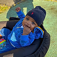 Ayden participe au concours pour gagner de l'argent avec cette photo : baby, child, stroller, blue_jacket, hat, beanie, outdoor, playground, shadow, fingers_in_mouth, cute, smiling, happy, person, infant, park, sunlight, clothing, seat, young