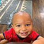 toddler, child, smile, red_shirt, anchor_pattern, face, indoor, wooden_floor, rug, happy, person, baby, cute, portrait, home, flooring, clothing, hand, expression, young_child