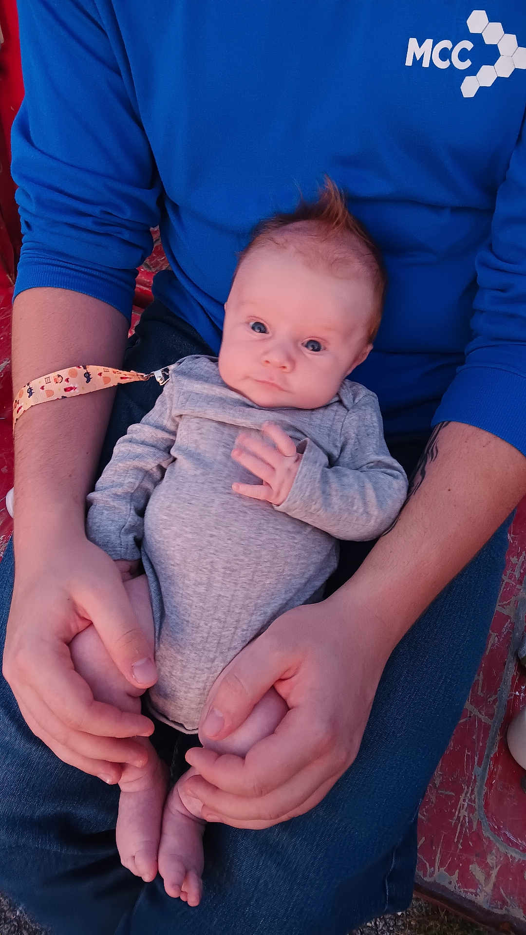 Thomas is registered to the contest to win money with this photo: baby, infant, person, hands, blue_shirt, holding, legs, gray_outfit, curious, mohawk, sitting, adult, skin, casual_clothing, outdoor, closeup, comfort, gentle, cute, portrait