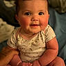 Kailani is registered to the contest to win money with this photo: baby, child, infant, smile, cute, onesie, rosy_cheeks, chubby, hands, sitting, portrait, face, eyes, indoors, soft_light, warm_tone, happy, person, closeup, young
