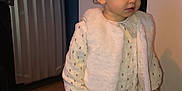 Inaya participe au concours pour gagner de l'argent avec cette photo : toddler, child, indoor, clothing, vest, boots, leggings, floor, curly_hair, standing, looking_away, winter_wear, brown_boots, white_vest, patterned_shirt, wooden_floor, suitcase, hanger, warm_clothing, person