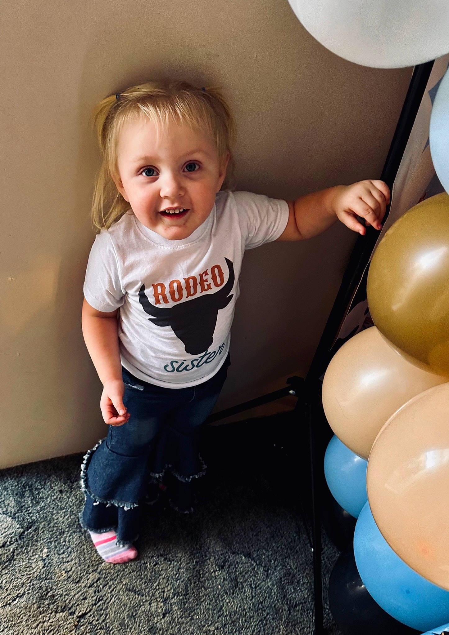 Bexley is registered to the contest to win money with this photo: arm, baby_toddler_clothing, balloon, child, event, flash_photography, fun, happy, human_body, human_leg, joy, leg, party_supply, person, sitting, skin, smile, standing, t_shirt, thigh
