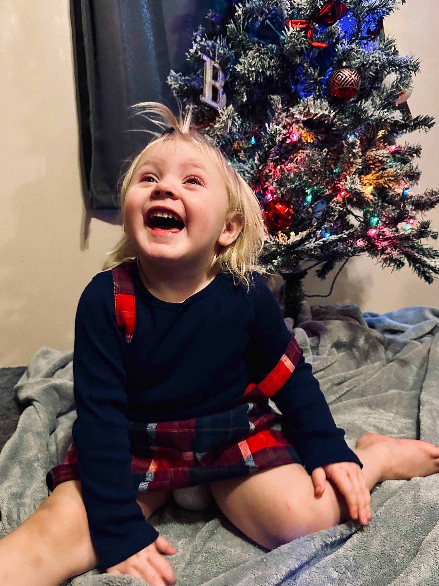 Bexley is registered to the contest to win money with this photo: baby_toddler_clothing, child, christmas_decoration, christmas_ornament, christmas_tree, dress, event, fun, happy, holiday, holiday_ornament, human_body, leg, ornament, person, plant, sitting, sleeve, smile, toddler