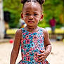 toddler, child, swimsuit, floral_pattern, outdoor, sand, hair_puffs, serious_expression, summer, playground, person, skin, earrings, standing, daylight, nature, blurred_background, colorful, portrait, young_child