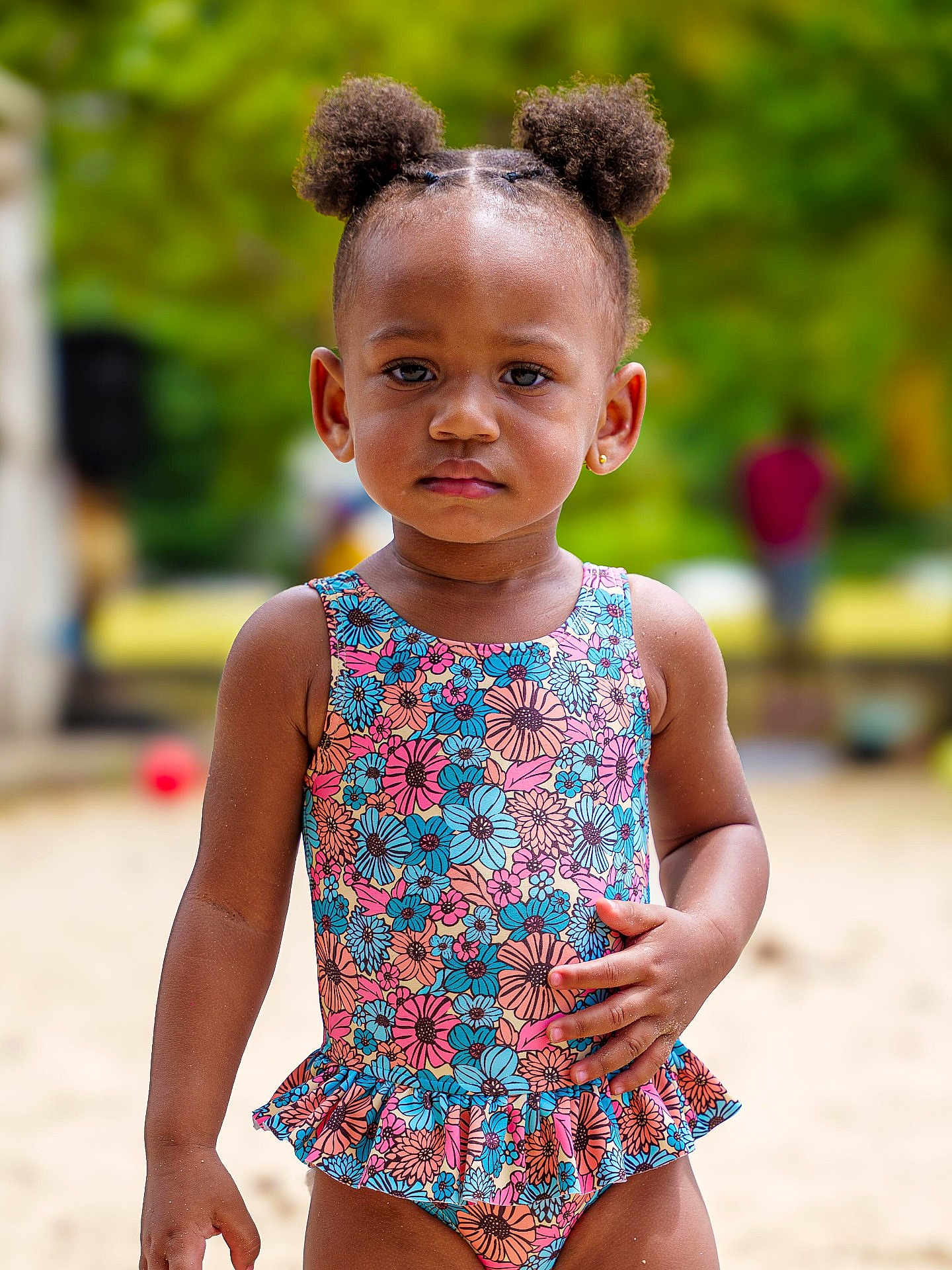 Naélyah participe au concours pour gagner de l'argent avec cette photo : toddler, child, swimsuit, floral_pattern, outdoor, sand, hair_puffs, serious_expression, summer, playground, person, skin, earrings, standing, daylight, nature, blurred_background, colorful, portrait, young_child