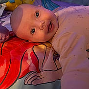 Lilith is registered to the contest to win money with this photo: baby, infant, child, face, smile, bedspread, colorful, plush_toy, bird_toy, cartoon, fabric, sleepwear, person, portrait, indoors, soft_light, cute, young, laying_down, closeup