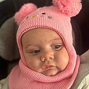 Jade a rejoint le concours — aidez-le/la à gagner de superbes lots ! baby, child, face, headwear, hat, knit, pom_poms, pink, warm_clothing, cute, infant, portrait, closeup, soft_texture, cozy, expression, person, young_child, indoors, seated