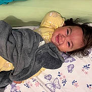 Avery is registered to the contest to win money with this photo: bed, bedroom, blanket, child, cozy, curly_hair, face, family, floral_bedding, gray_blanket, happy, indoors, lying_down, pajamas, pillow, portrait, smiling, snuggling, toddler, yellow_clothing