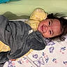 bed, bedroom, blanket, child, cozy, curly_hair, face, family, floral_bedding, gray_blanket, happy, indoors, lying_down, pajamas, pillow, portrait, smiling, snuggling, toddler, yellow_clothing