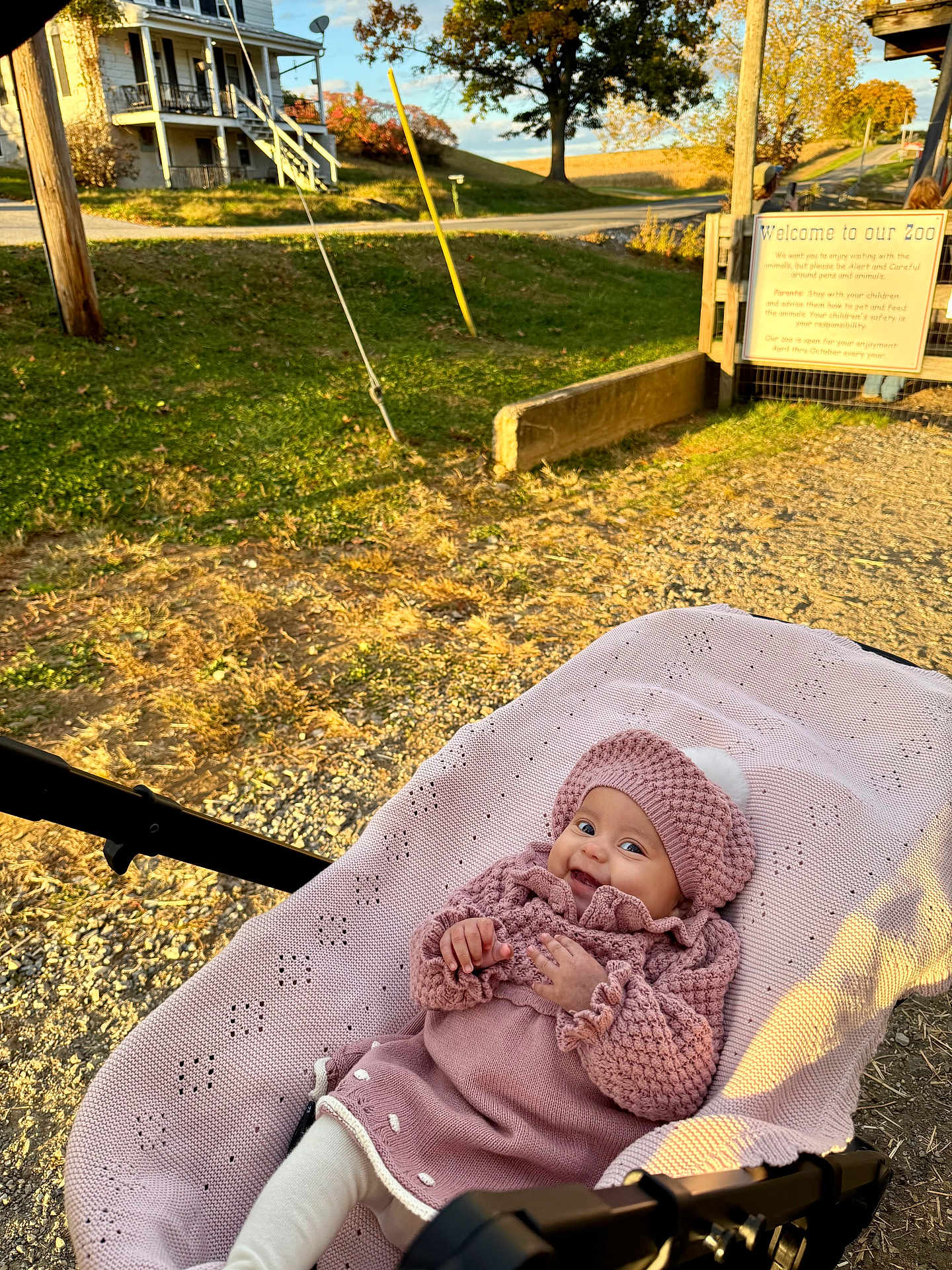 Mía Issabela is registered to the contest to win money with this photo: baby, stroller, pink_clothing, knit_hat, knit_sweater, blanket, outdoor, sunlight, smile, happy, grass, road, sign, tree, house, fence, child, nature, daylight, park
