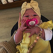 Charly a rejoint le concours — aidez-le/la à gagner de superbes lots ! baby, pacifier, headband, yellow_clothing, hand, crib, blanket, wooden_floor, pacifier_clip, beads, toddler, indoors, person, child, cute, sitting, knit_blanket, infant, face, clothing