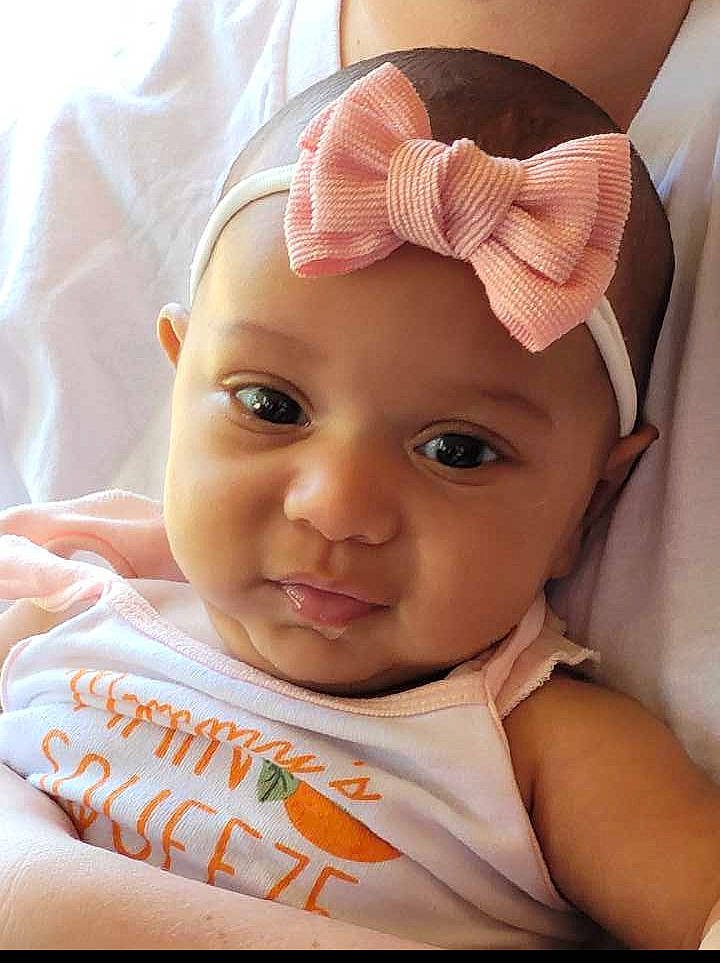 Genevieve is registered to the contest to win money with this photo: baby, baby_toddler_clothing, cheek, child, comfort, ear, eyebrow, eyelash, fashion_accessory, happy, headband, headgear, headpiece, headwear, linens, lip, person, pink, skin, sleeve