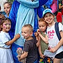 Luna a rejoint le concours — aidez-le/la à gagner de superbes lots ! children, mascot, costume, blue, face_paint, teddy_bear, outdoor, smiling, group, summer, casual_clothing, footwear, hat, backpack, building, pavement, fence, playful, happy, posing