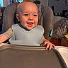 baby, bib, child, clothing, cute, face, feeding, furniture, hand, happy, high_chair, home, indoor, infant, kitchen, mealtime, person, smiling, table, young_child