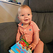 Kash joined the competition — help win amazing prizes! baby, child, smiling, indoor, chair, book, reading, shirt, plaid, happy, face, hand, foot, furniture, window, light, colorful, young, person, portrait