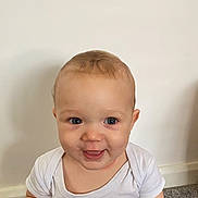 Cole is registered to the contest to win money with this photo: baby, child, infant, face, blue_eyes, white_onesie, smiling, indoor, carpet, wall, head, skin, young, cute, portrait, person, happy, childhood, human, sitting