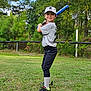 child, baseball, bat, sports_uniform, cap, grass, outdoor, athlete, young, field, trees, smile, sneakers, sport, player, greenery, fence, pose, recreation, daylight