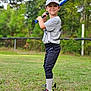 child, baseball, bat, sportswear, cap, smiling, outdoor, grass, field, athlete, young, pose, confidence, tree, fence, sneakers, socks, daylight, portrait, recreation