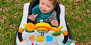 Lucas is registered to the contest to win money with this photo: baby, baby_walker, child, grass, outdoor, toy, smile, happy, play, infant, person, greenery, walker, colorful, cute, young_child, sitting, clothing, plaything, nature