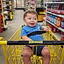 aisle, baby, blue_shirt, child, clothing, feet, grocery, happy, indoor, legs, person, retail, seatbelt, shopping, shopping_cart, smiling, store, supermarket, toddler, yellow_cart