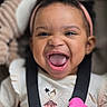 Egypt is registered to the contest to win money with this photo: baby, child, infant, portrait, smiling, laughing, tongue, pink_bow, headband, curly_hair, black_hair, baby_seat, harness, tablet_case, pink, clothing, dress, indoor, close_up, happy