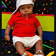 Cam'Ron is registered to the contest to win money with this photo: baby, child, red_shirt, white_shorts, white_cap, brown_shoes, carpet, colorful_background, sitting, serious_expression, indoor, portrait, footwear, hat, person, patterned_floor, cute, fashion, casual_clothing, infant