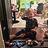 toddler, child, smiling, indoor, pajamas, toys, toy_cars, wooden_floor, christmas_tree, holiday_decor, cat, orange_cat, holiday_lights, happy, playtime, floor, animal, home, cute, festive