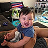 Ezra joined the competition — help win amazing prizes! baby, child, infant, smiling, happy, portrait, indoors, living_room, sofa, adult, arms, blue_shirt, toys, playmat, television, cushions, family, sitting, home, photography