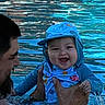 baby, child, infant, adult, parent, smiling, happy, blue_clothing, cap, pool, water, swimming, outdoor, portrait, close_up, holding, family, face, ripples, summer