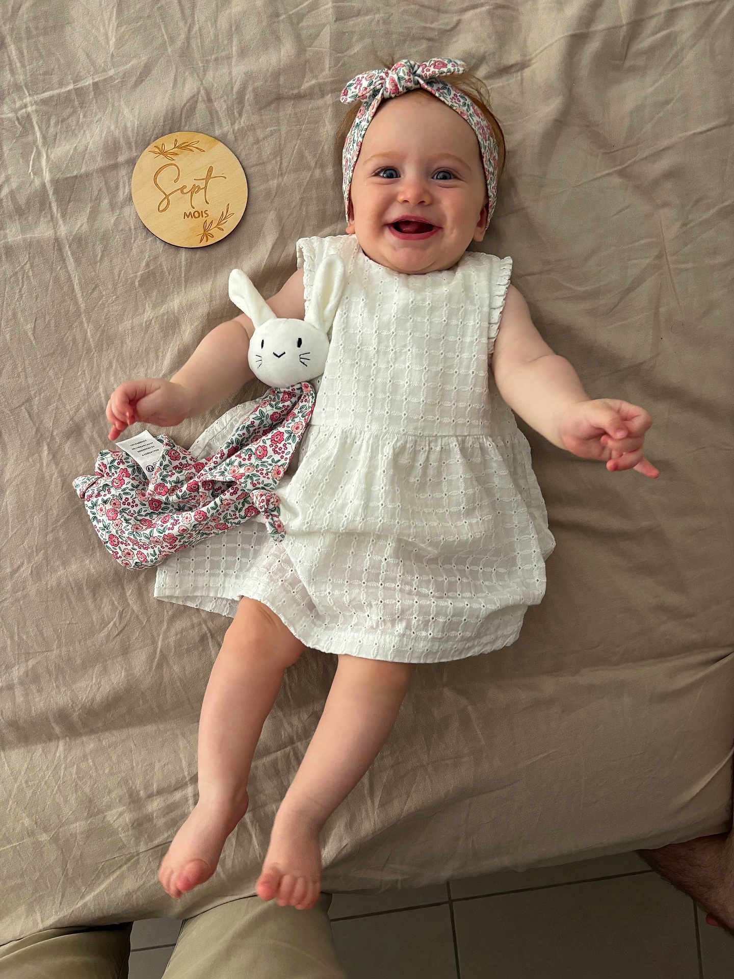 Albane a rejoint le concours — aidez-le/la à gagner de superbes lots ! baby, infant, smiling, white_dress, headband, plush_toy, bunny, bed, blanket, wooden_plaque, milestone, cute, happy, child, indoors, person, feet, hands, fabric, portrait