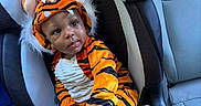 Major is registered to the contest to win money with this photo: baby, child, tiger_costume, tiger, car_seat, car, infant, portrait, sitting, indoors, vehicle, orange, striped_clothing, furry_hood, costume, serious_expression, headwear,  안전, photography, adorable