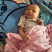 Tyanna joined the competition — help win amazing prizes! baby, infant, child, smiling, portrait, lying_down, blanket, pink_blanket, floral_clothing, cartoon_bedding, bed, cozy, indoors, face, hands, eyes, brown_hair, happy, candid, close_up