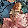 baby, infant, child, smiling, portrait, lying_down, blanket, pink_blanket, floral_clothing, cartoon_bedding, bed, cozy, indoors, face, hands, eyes, brown_hair, happy, candid, close_up
