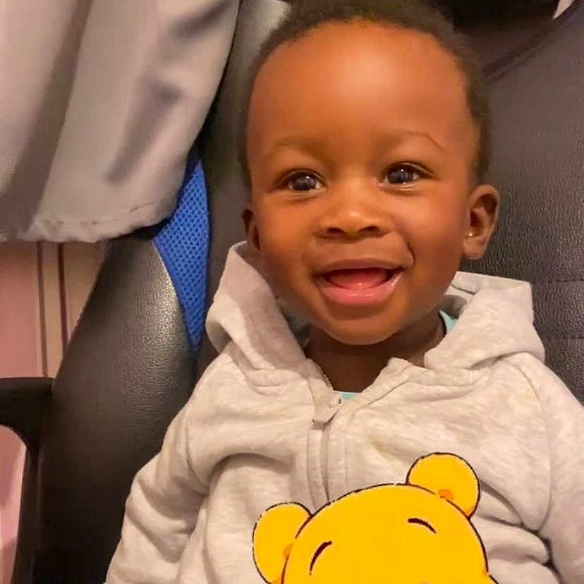 Rayan Hakim a rejoint le concours — aidez-le/la à gagner de superbes lots ! black_hair, camo_pants, casual_clothing, chair, child, cozy, cute, expression, graphic, happy, hoodie, indoor, person, playful, portrait, seated, smiling, toddler, winnie_the_pooh, young_child