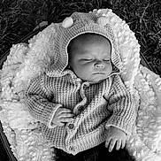 Max is registered to the contest to win money with this photo: baby, infant, sleeping, knit_sweater, hood, pom_poms, blanket, basket, outdoor, grass, black_and_white, peaceful, cozy, texture, portrait, newborn, child, soft_lighting, hands, resting