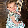 child, toddler, smiling, floral_dress, wooden_floor, baby_gate, indoor, cute, sitting, happy, person, home, flooring, infant, young_child, bright_eyes, casual_clothing, domestic, portrait, baby