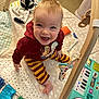 baby, child, smiling, sitting, play_mat, toys, hoodie, striped_pants, indoor, carpet, colorful, happy, cute, infant, playtime, person, face, young_child, floor, wooden_frame