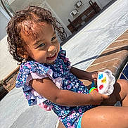 Kaydance joined the competition — help win amazing prizes! toddler, child, smile, curly_hair, floral_swimsuit, toy, poolside, sunlight, outdoor, water, playful, happy, summer, skin, legs, concrete, brick, casual, daytime, person