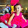 toddler, child, pink_dress, headband, spoon, sitting, wooden_surface, flowers, blurred_background, indoor, person, cute, happy, playful, portrait, bright_colors, innocence, curiosity, seated, baby