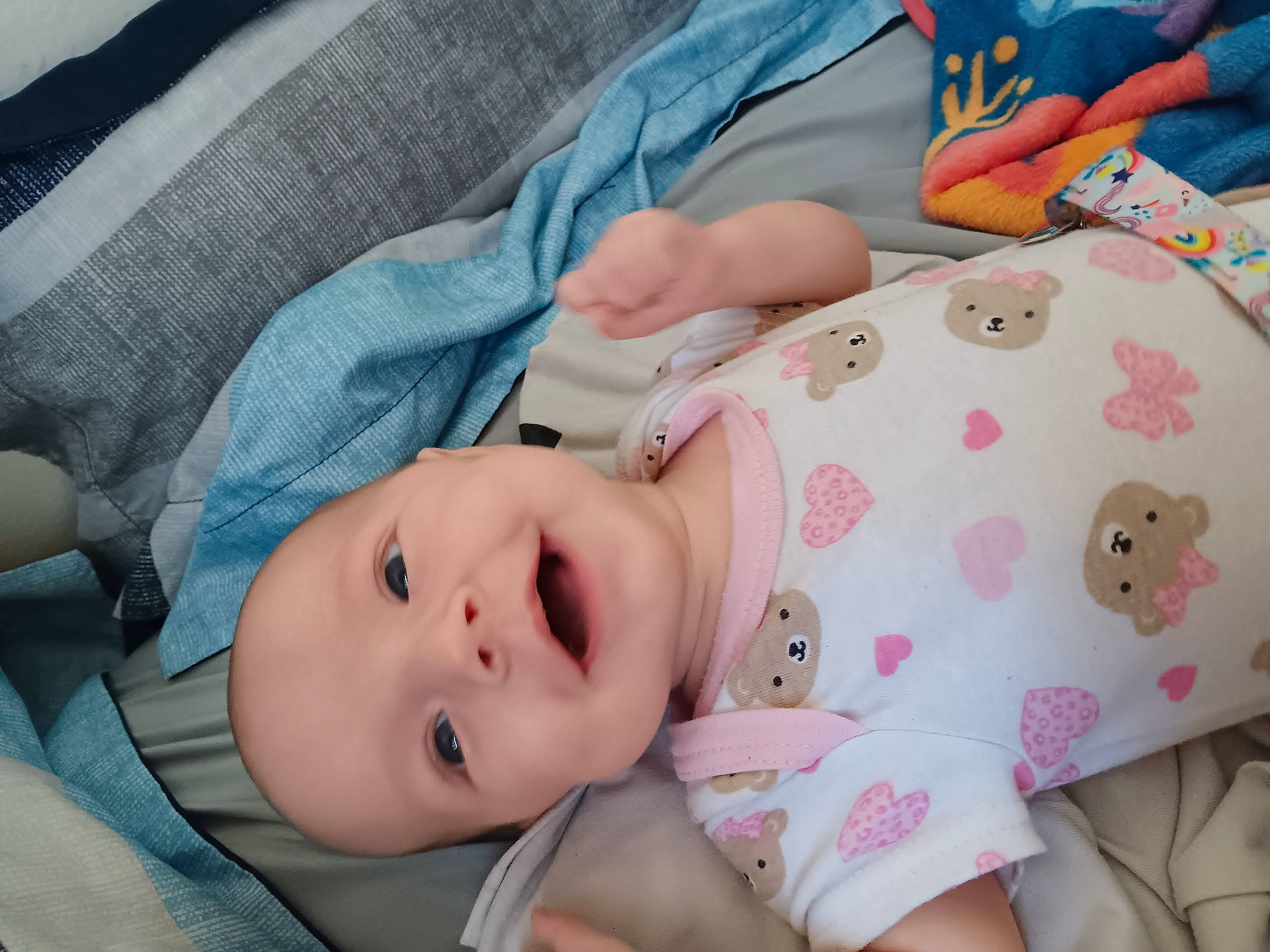 Fiona is registered to the contest to win money with this photo: baby, bed, blanket, child, clothing, cute, face, happy, head, heart_pattern, indoor, infant, lying_down, onesie, person, portrait, skin, smile, soft_fabric, teddy_bear_pattern