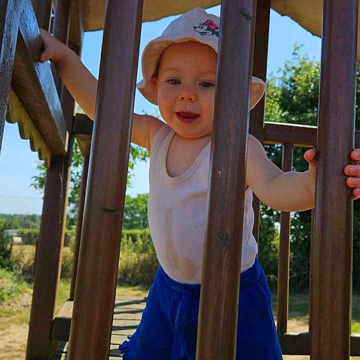 Djulya a rejoint le concours — aidez-le/la à gagner de superbes lots ! barefoot, child, daytime, greenery, happy, hat, nature, outdoor, person, play, playground, shorts, smiling, standing, summer, sunny, tank_top, toddler, wood, wooden_bars
