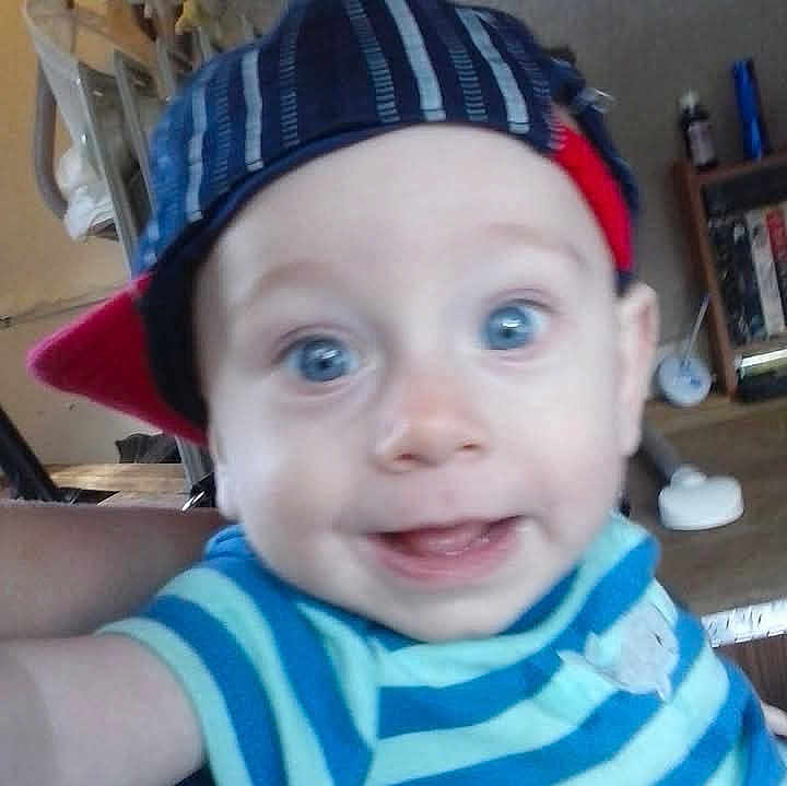 Christopher is registered to the contest to win money with this photo: baby, child, blue_eyes, striped_shirt, cap, smiling, close_up, indoor, person, face, happy, young_child, headwear, casual_clothing, portrait, cheerful, infant, home, cute, expression