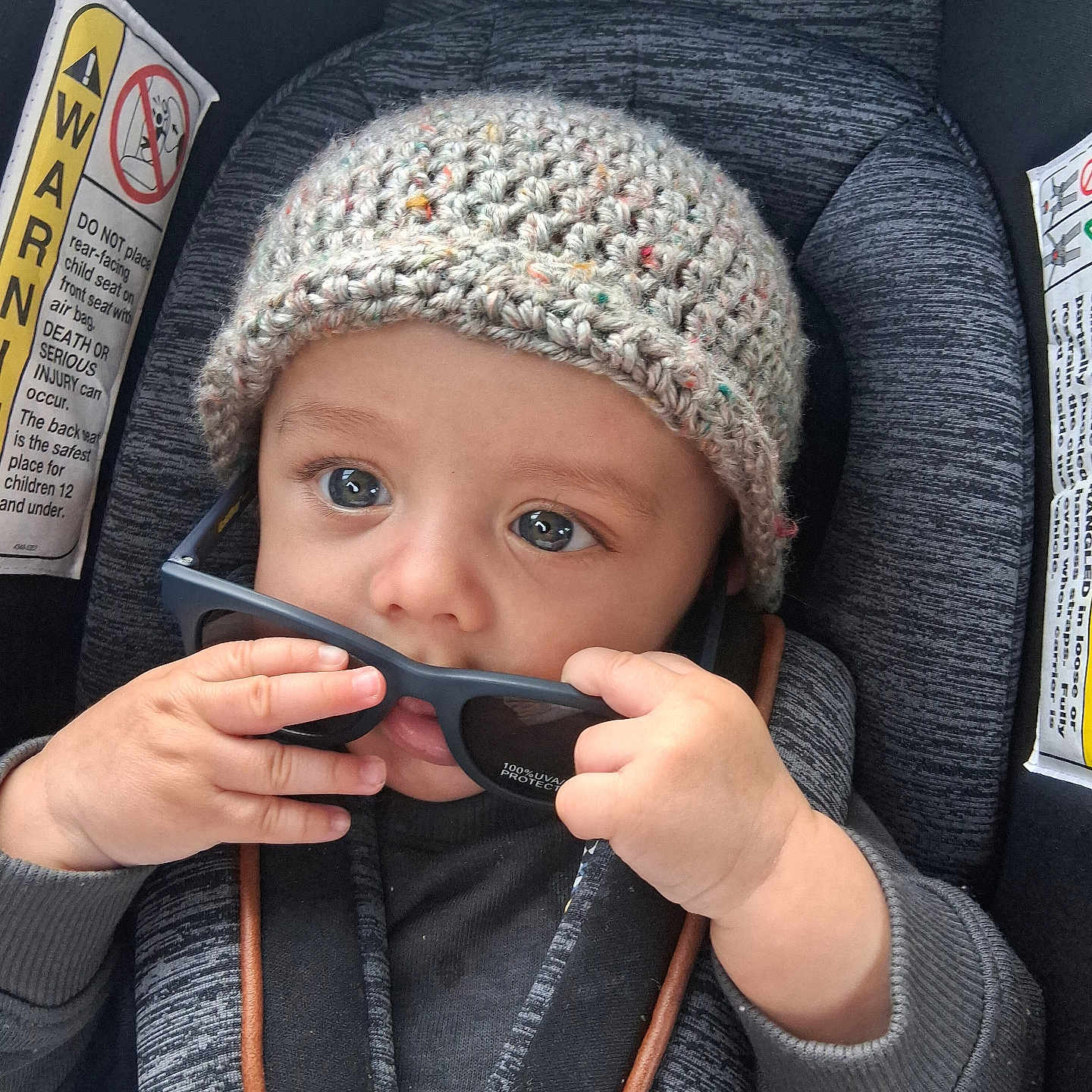 Angel Santos is registered to the contest to win money with this photo: baby, child, car_seat, knitted_hat, sunglasses, hands, blue_eyes, cute, infant, seat_belt, clothing, portrait, indoor, person, young_child, closeup, curious, playing, seat, safety