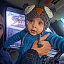 baby, child, owl_hat, knitted_hat, blue_clothing, hand, car_interior, rain, window, steering_wheel, adult, person, face, eyes, cute, winter_clothing, vehicle, seat, seatbelt, closeup