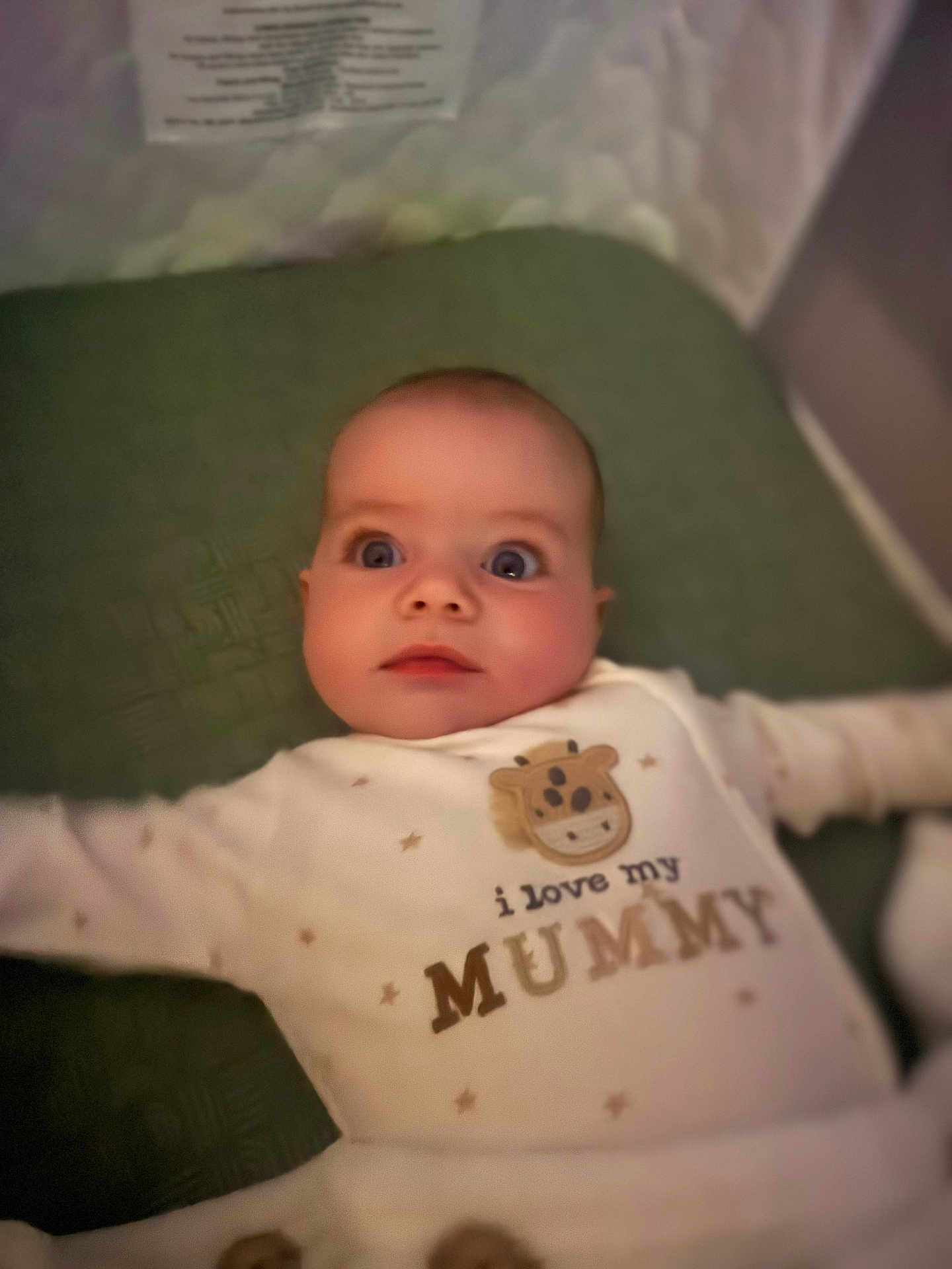 Cole joined the competition — help win amazing prizes! baby, infant, onesie, text_on_clothing, love_mummy, lying_down, green_surface, wide_eyes, cute, child, portrait, indoor, soft_lighting, small_person, adorable, face, expression, clothing, sleepwear, newborn