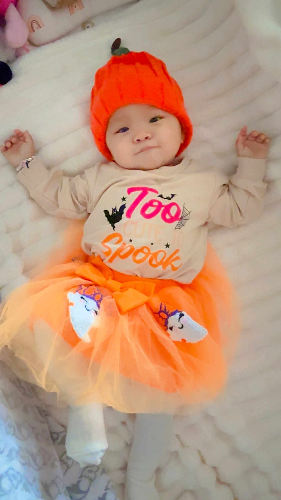 Nuyangma is registered to the contest to win money with this photo: baby, infant, tutu, orange_hat, pumpkin_hat, white_blanket, cute, lying_down, child, festive_clothing, shirt, text_on_shirt, soft_texture, indoors, sleepwear, costume, happy, smiling, portrait, toddler